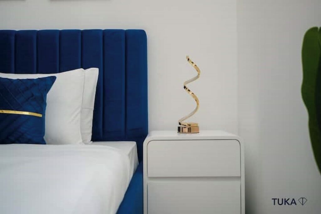 Un letto con una testiera blu, biancheria da letto bianca e un oggetto decorativo sul comodino.