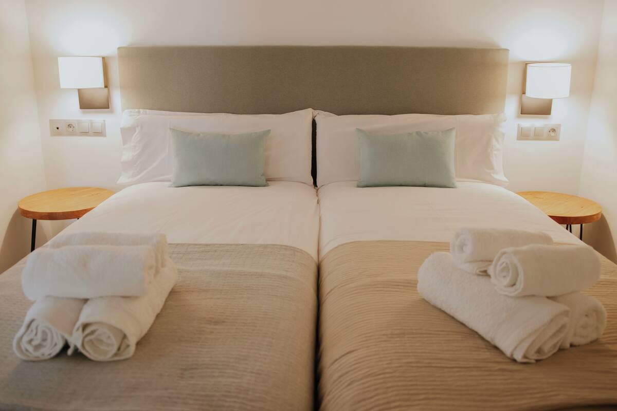 A double room with two beds, each with a headboard, two pillows, and two nightstands with lamps.