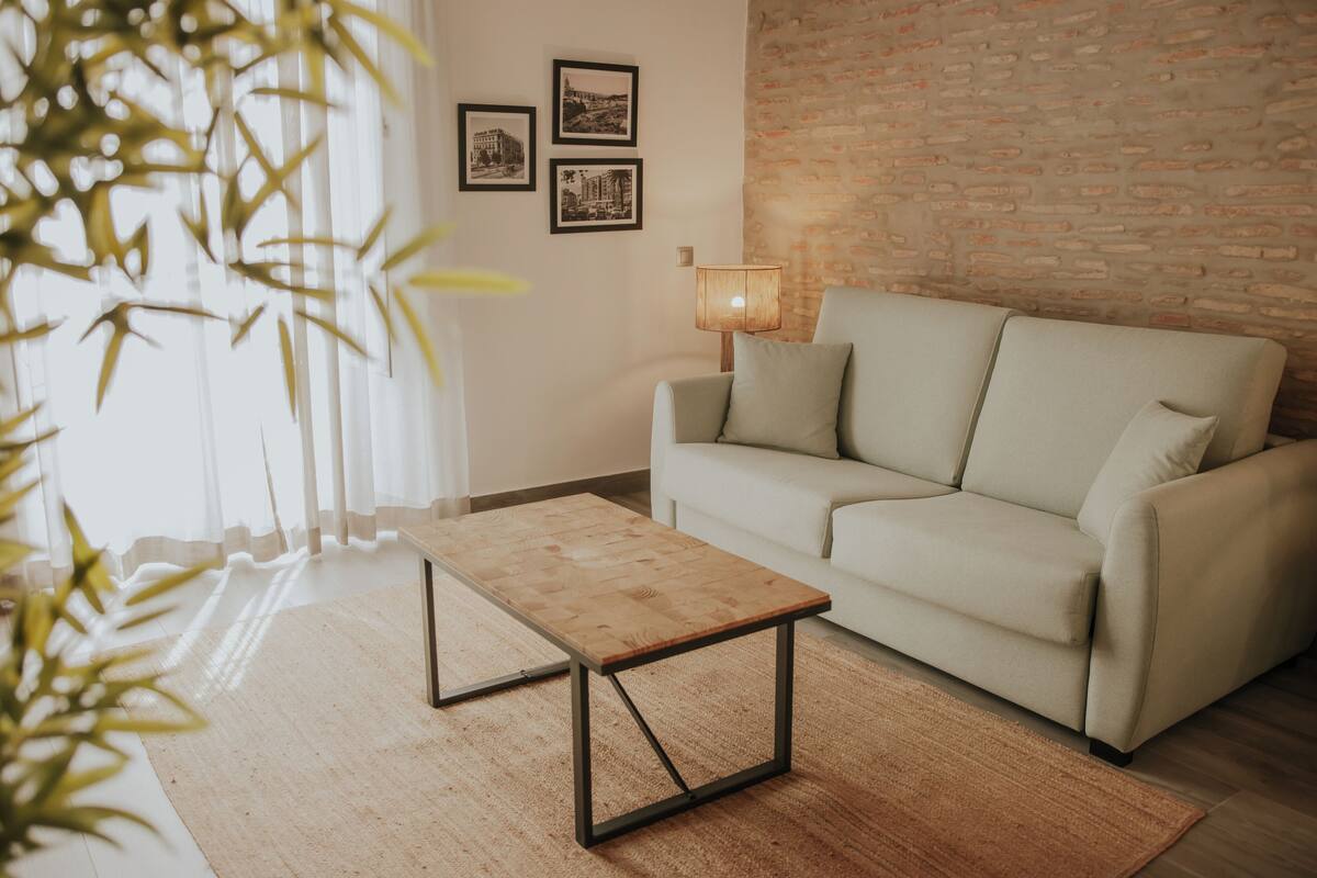 A living room with a light-colored sofa, a wooden coffee table, a lamp, and a brick wall.