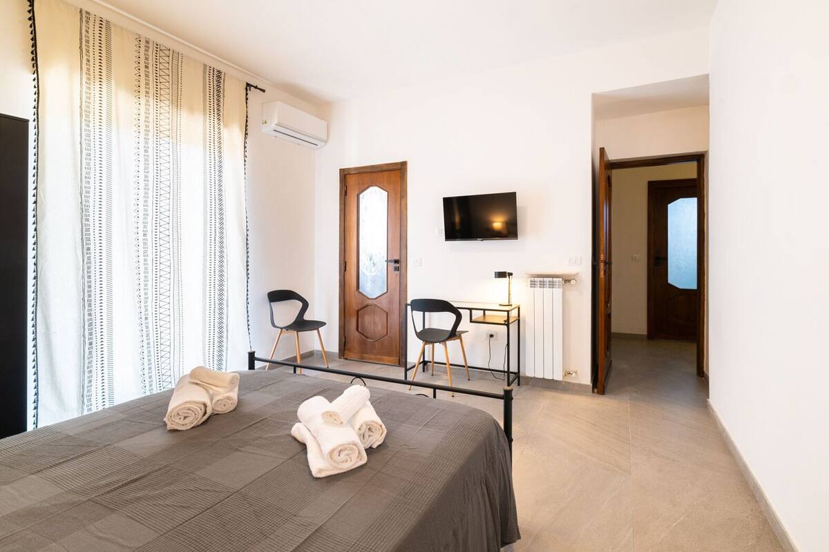 Ein Hotelzimmer mit einem Bett, zwei Stühlen, einem Schreibtisch, einem Fernseher und einer Klimaanlage.