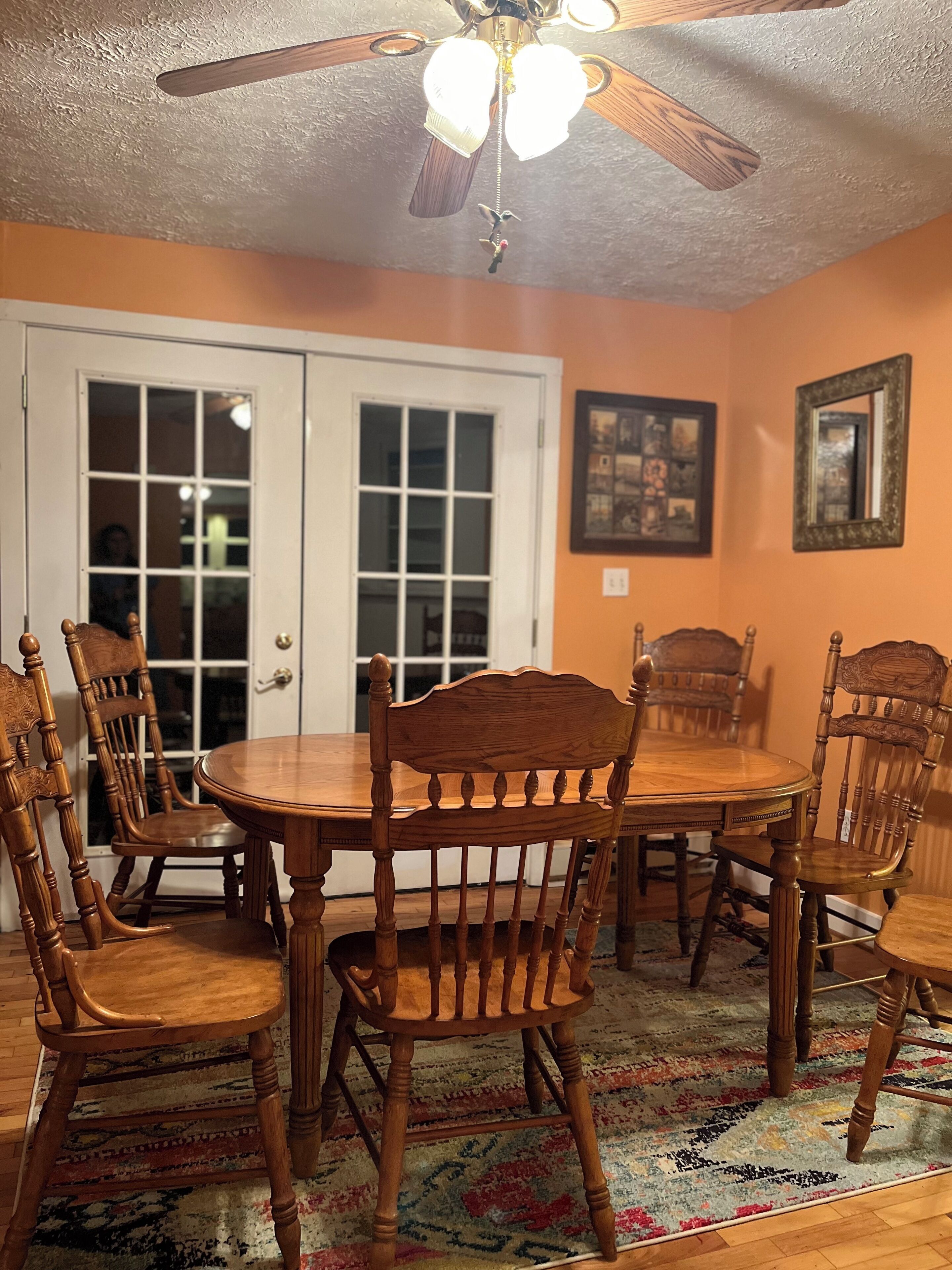 A dining room with a wooden table and chairs, a ceiling fan, and a patterned rug.