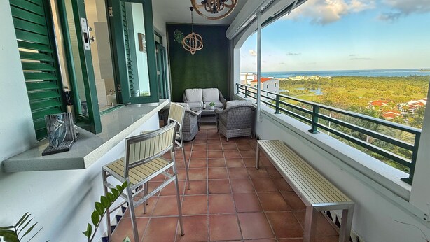Ein Balkon mit Blick auf einen Golfplatz und den Ozean. Es sind Korbstühle und ein kleiner Tisch vorhanden.