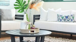 Ein modernes Wohnzimmer mit einem runden schwarzen Couchtisch, einem weißen Sofa mit gemusterten Kissen und einer großen grünen Pflanze in einer weißen Vase.