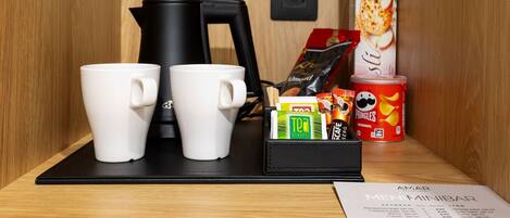 Una estación de café con dos tazas blancas, una cafetera negra, una caja de té, una lata de Pringles y un menú.