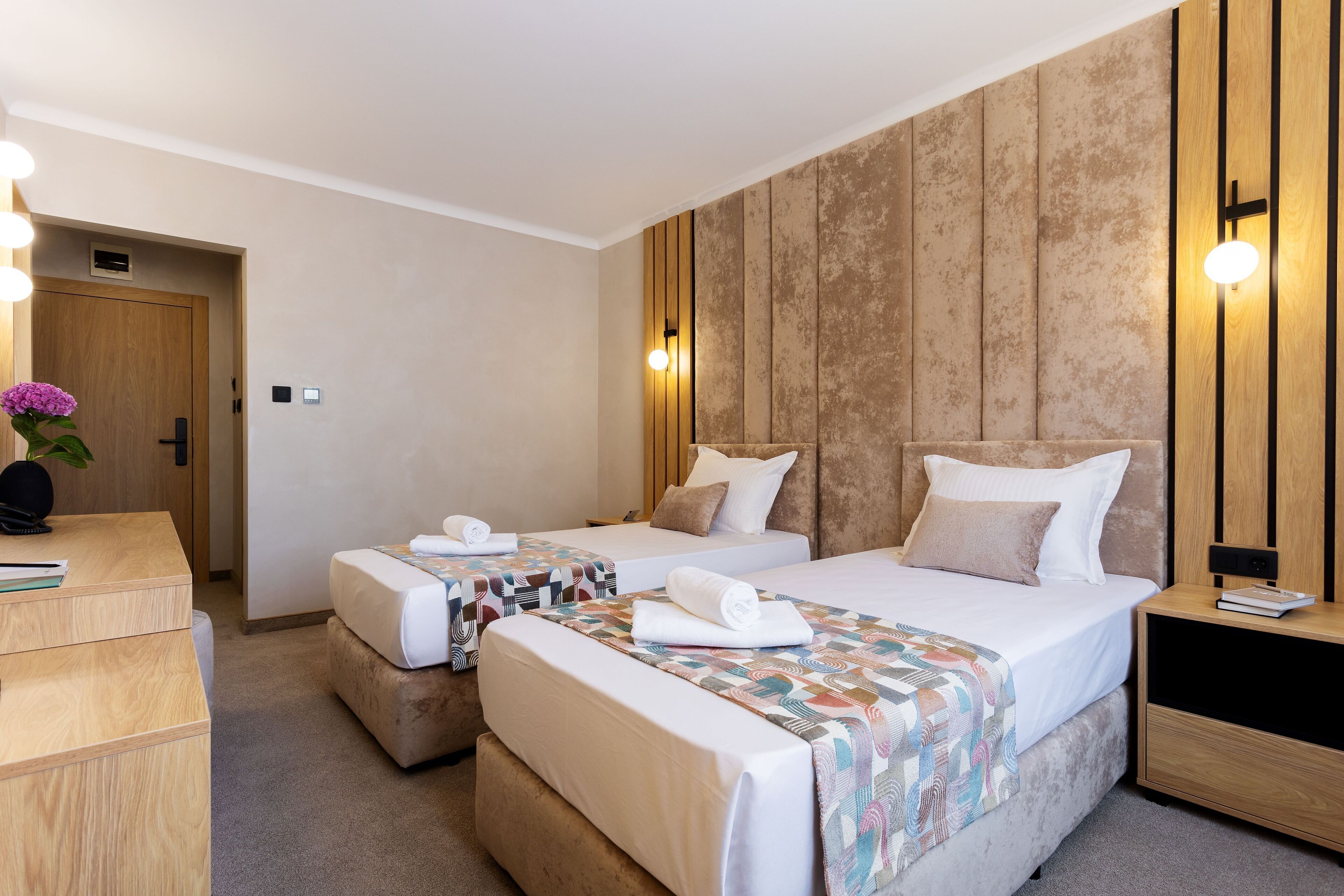 Ein Hotelzimmer mit zwei Betten, einem Holztisch und einem Nachttisch.
