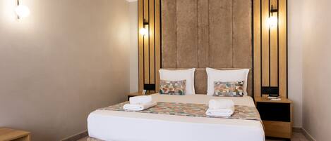 Une chambre d’hôtel avec un grand lit, une tête de lit en bois, des tables de chevet et des lampes fixées au mur.