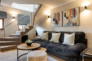 A modern living room with a staircase, a dark grey sofa, a round coffee table, and a wall-mounted artwork.