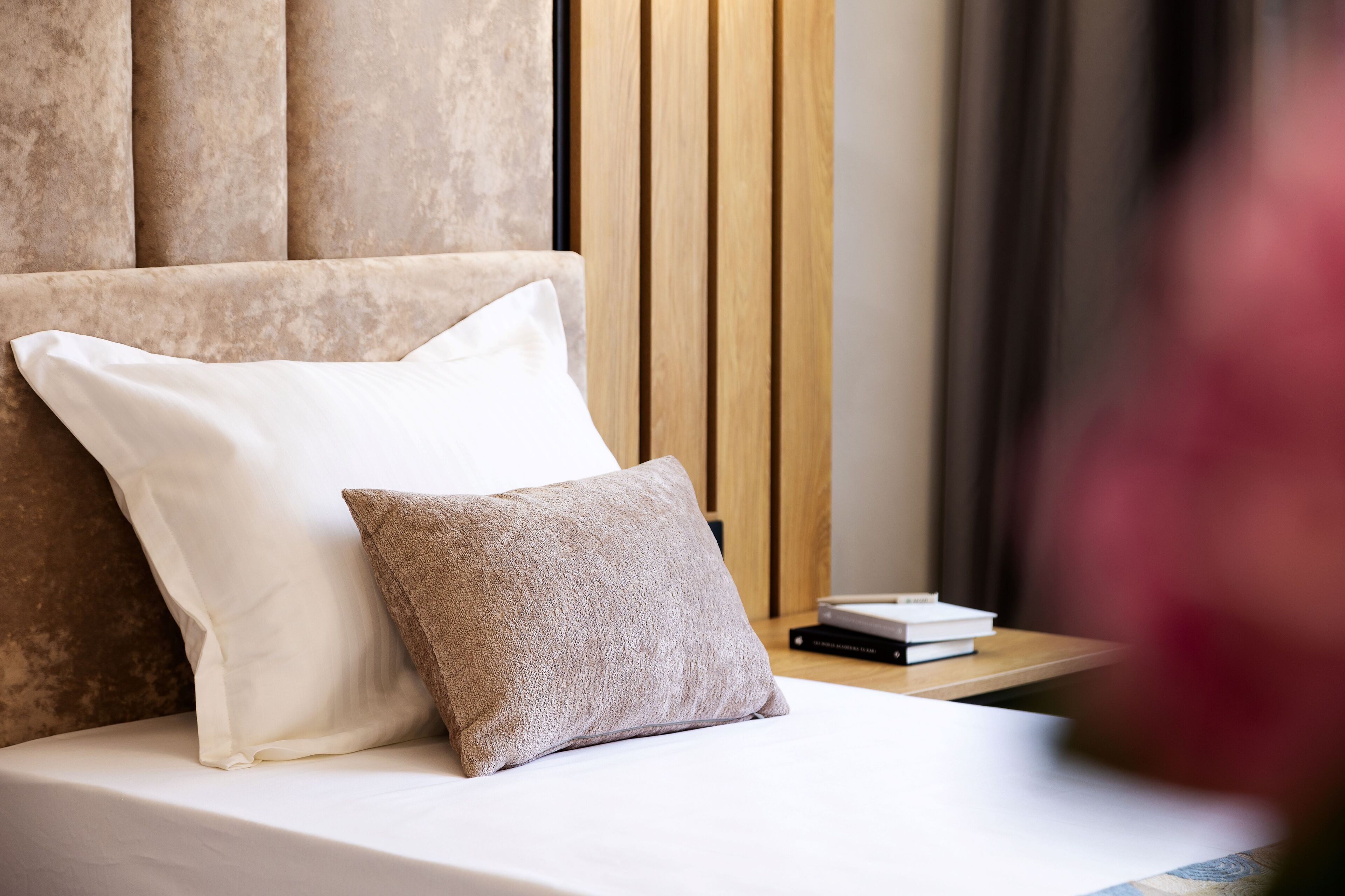 A neatly made bed with two pillows, a wooden headboard, and a small bedside table with books.