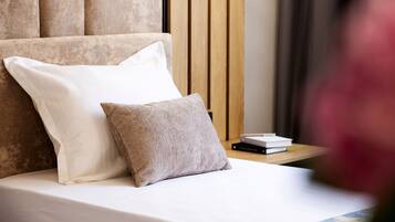 A neatly made bed with two pillows, a wooden headboard, and a small bedside table with books.