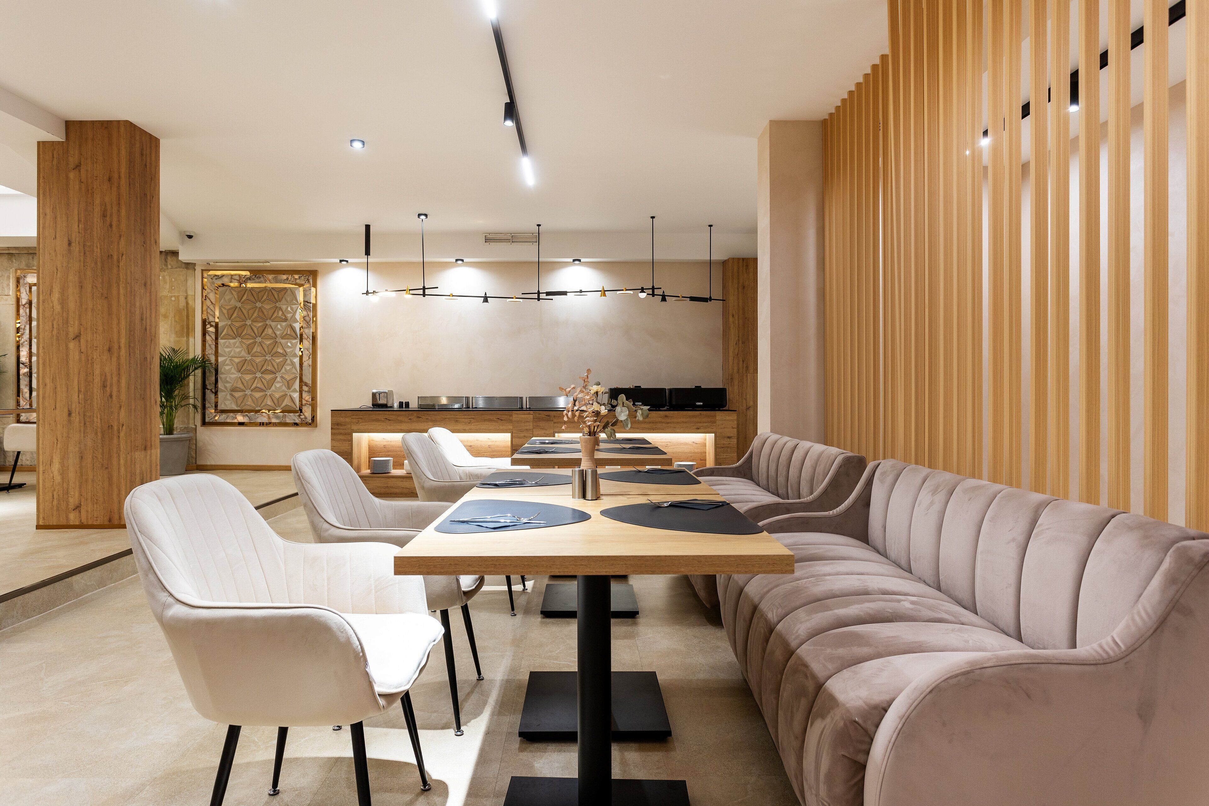 A modern dining area with a long table, cushioned chairs, and a sofa.