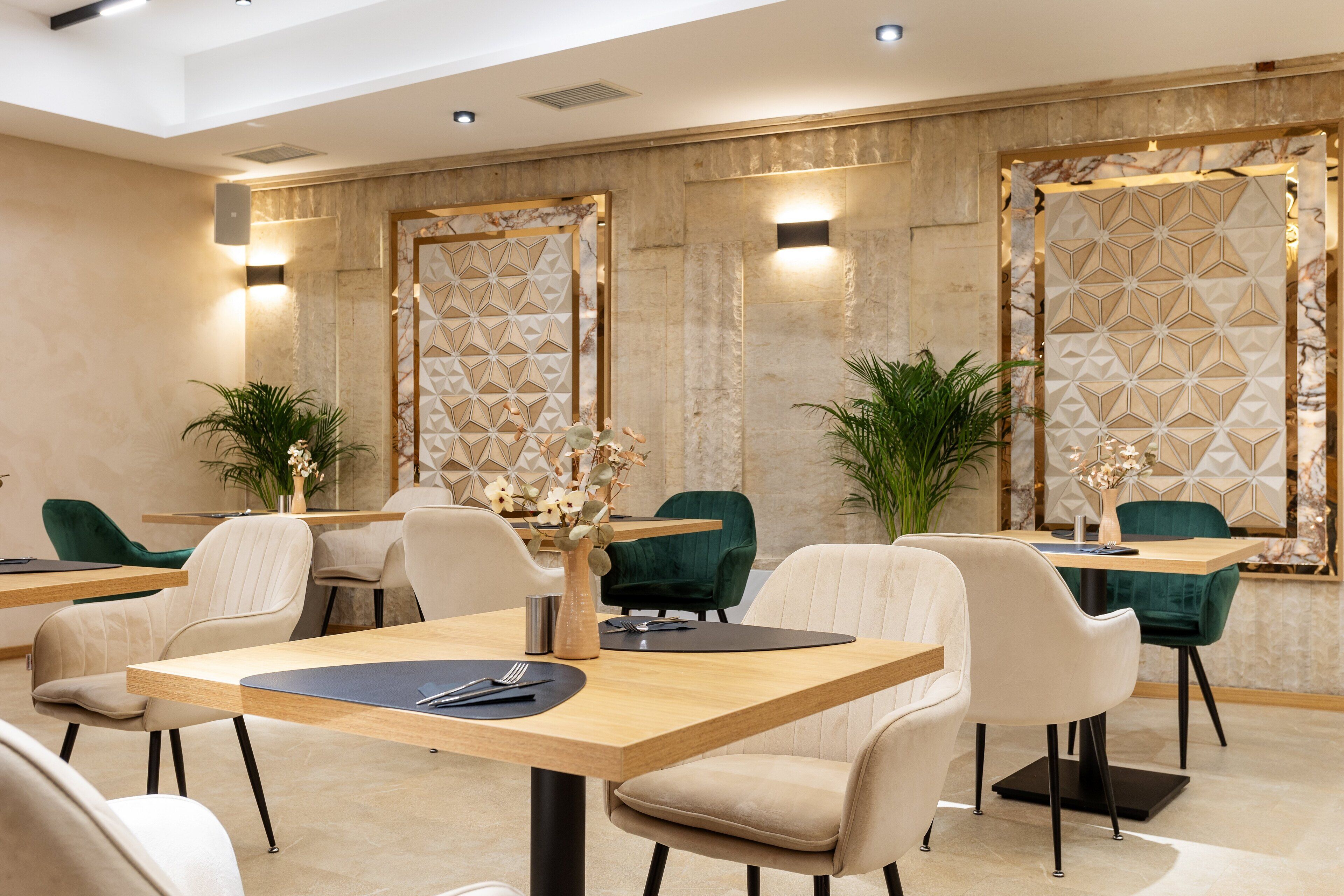 Ein moderner Hotel-Speisebereich mit geometrischen Wandgestaltungen, einer Mischung aus grünen und beigen Stühlen sowie einem zentralen Holztisch.