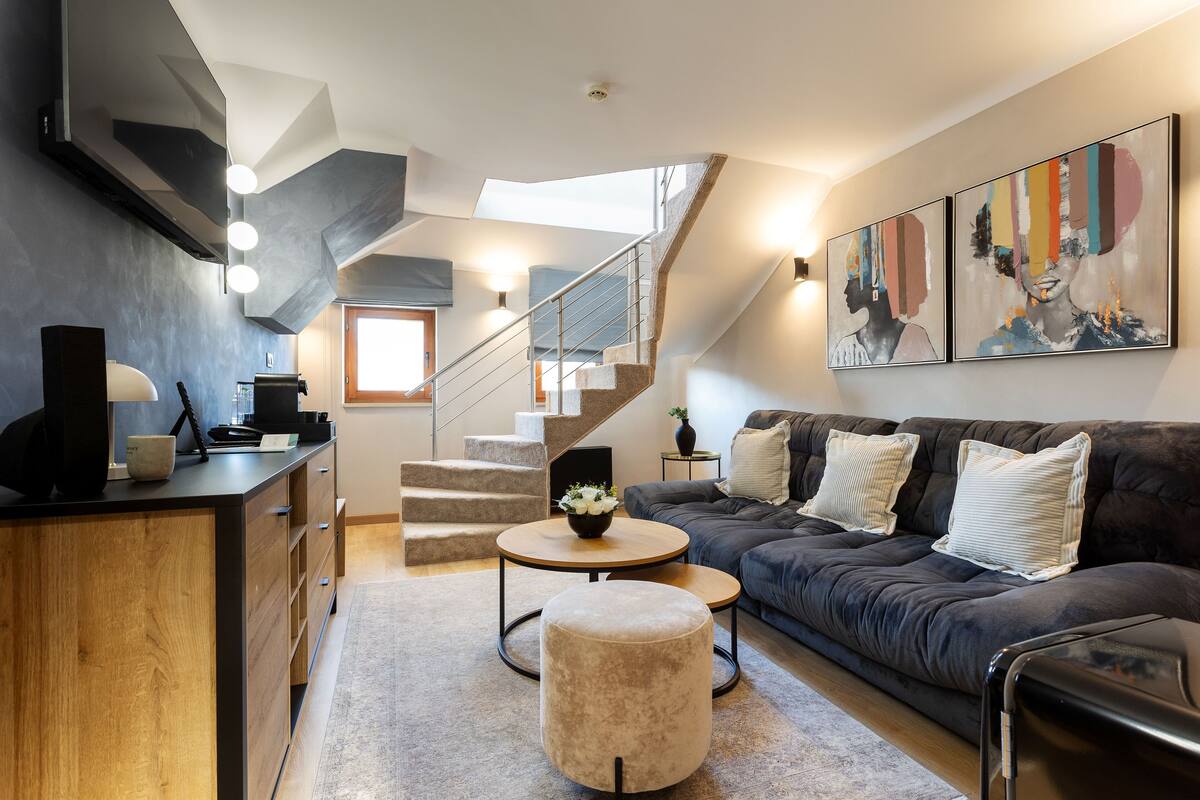 A modern living room with a staircase, a sofa, a coffee table, and artwork on the wall.
