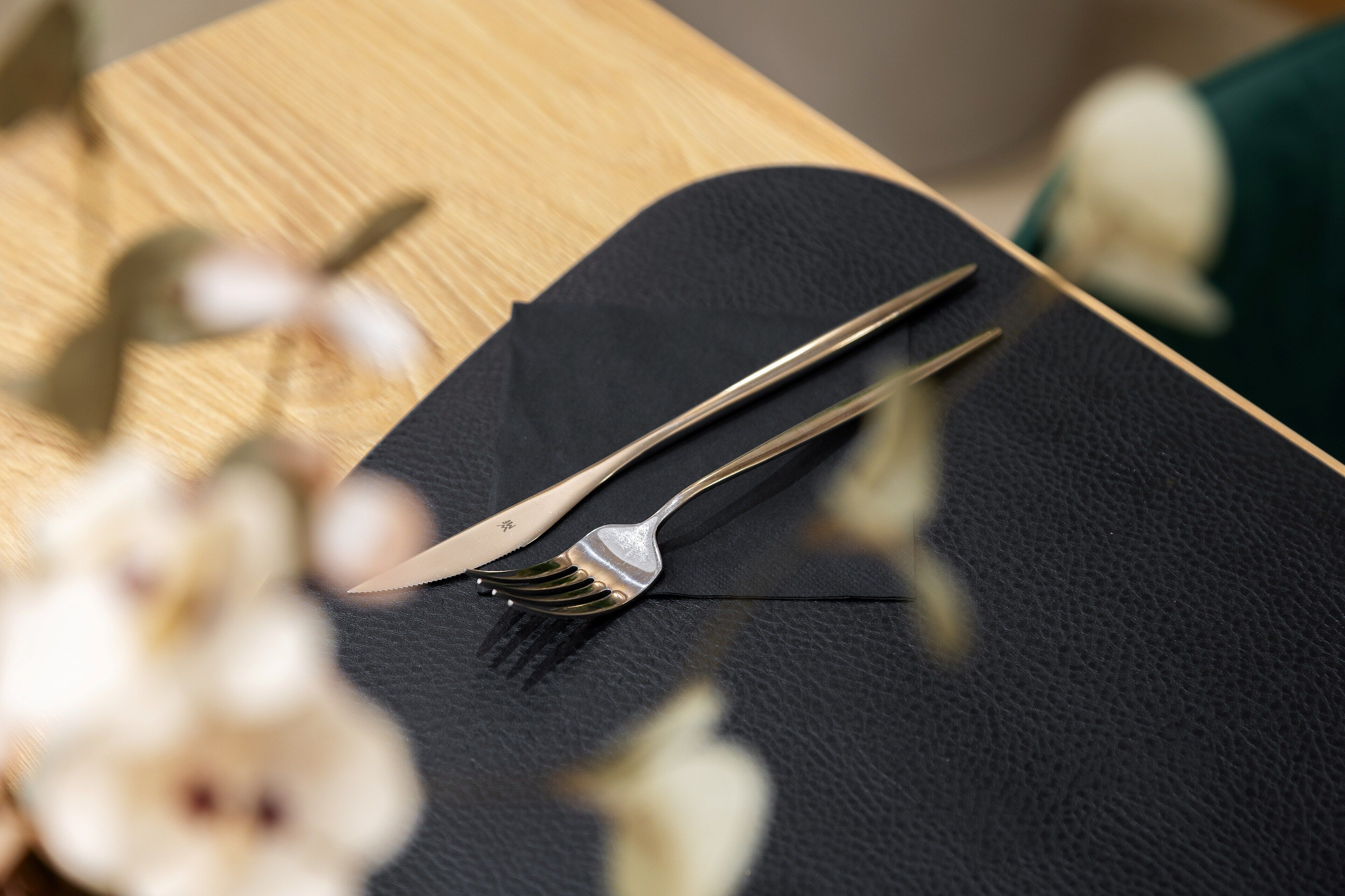 A black tablecloth with a fork and knife on a wooden table.