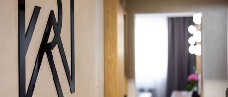 A modern interior with a minimalist design, featuring a large black letter 'K' on the wall, a wooden door, and a bright light fixture.