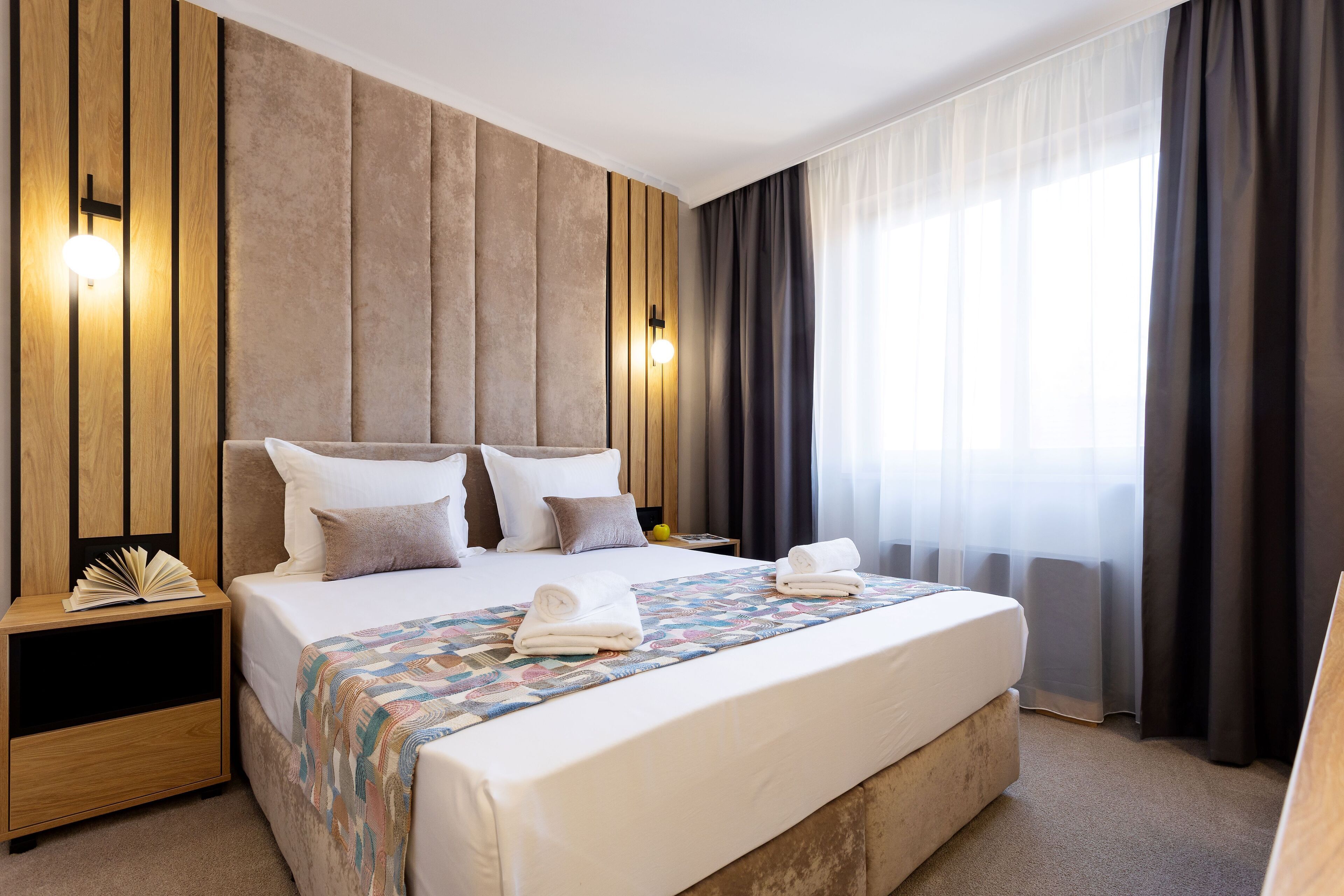 A modern hotel room with a large bed, a wooden headboard, and a nightstand with a lamp.