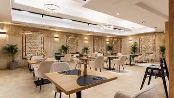 A modern dining area with multiple tables and chairs, geometric wall patterns, and chandeliers.