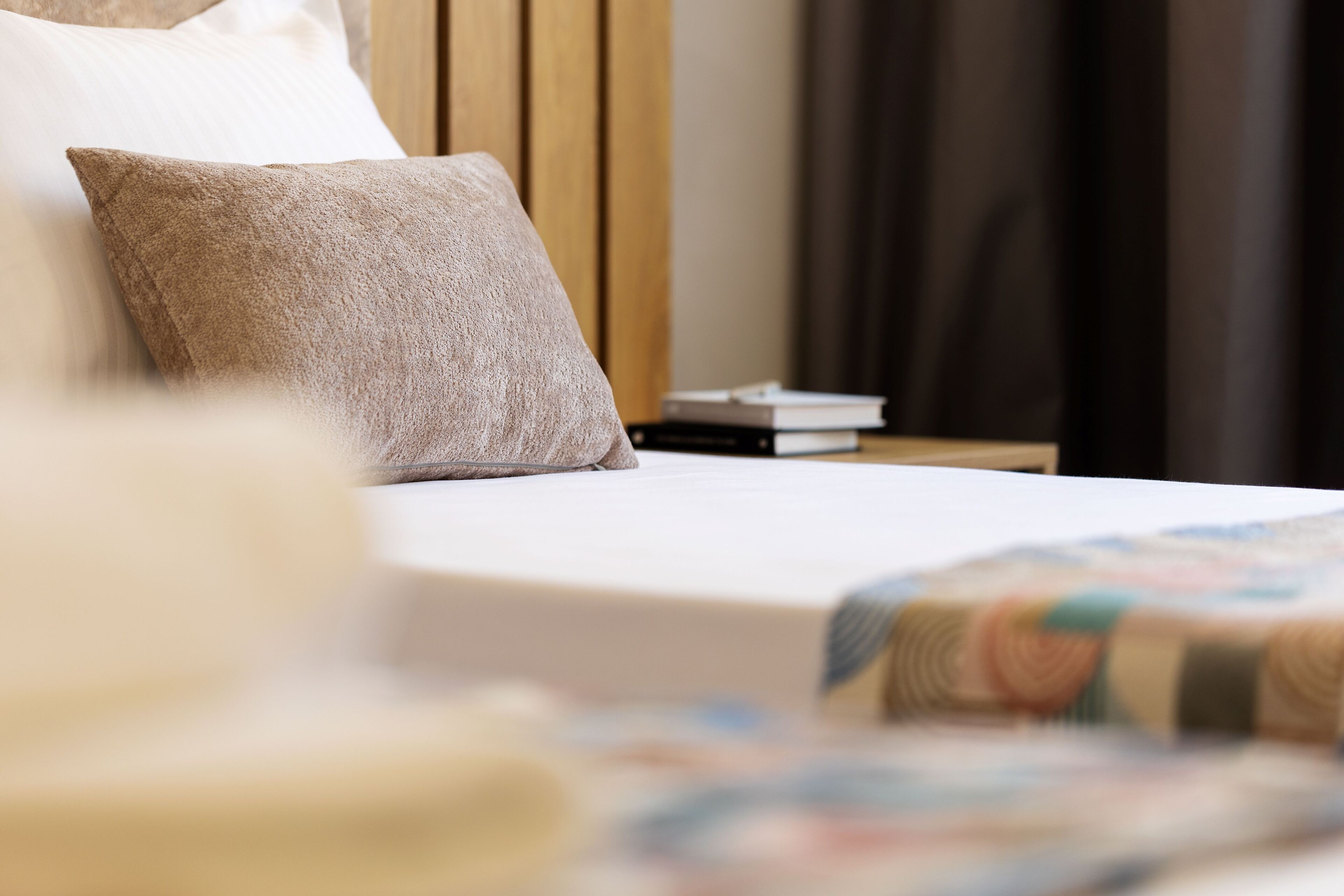 A neatly made bed with a pillow and a quilt, a wooden headboard, and a nightstand with books.
