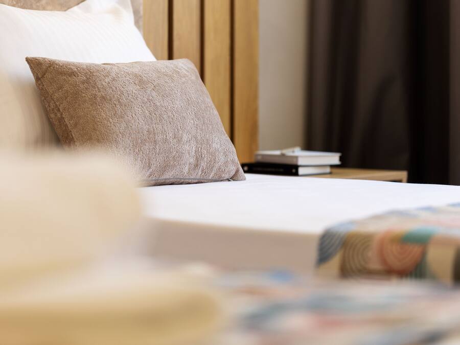 A neatly made bed with a pillow and a quilt, a wooden headboard, and a nightstand with books.