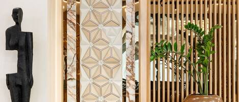 A modern interior with a marble floor, a geometric patterned door, a tall plant in a vase, and a black abstract sculpture.