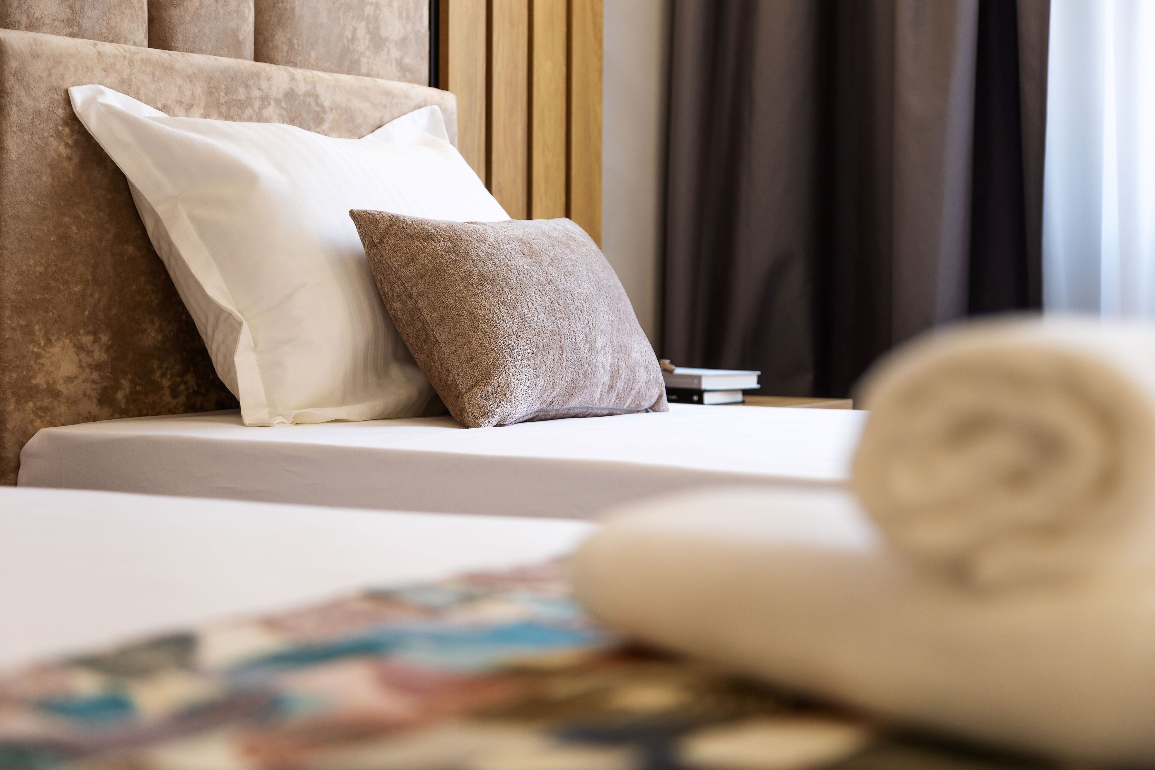 A neatly made bed with two pillows, a rolled towel, and a small bedside table.