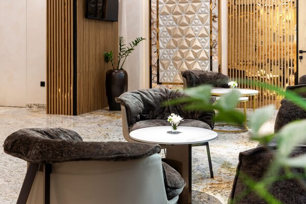 A modern lounge area with a sofa, armchair, and small round table, featuring a decorative vase with a flower. - AMAR Design Hotel by HMG (Sofia)
