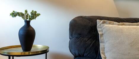 A dark-colored sofa with a textured cushion and a round side table with a dark vase containing green plants.
