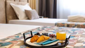 Bandeja de desayuno con croissants, frutos rojos y jugo de naranja sobre un mantel estampado en una habitación de hotel.