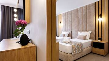 A modern hotel room with a wooden desk, a bed with a beige headboard, and a nightstand.