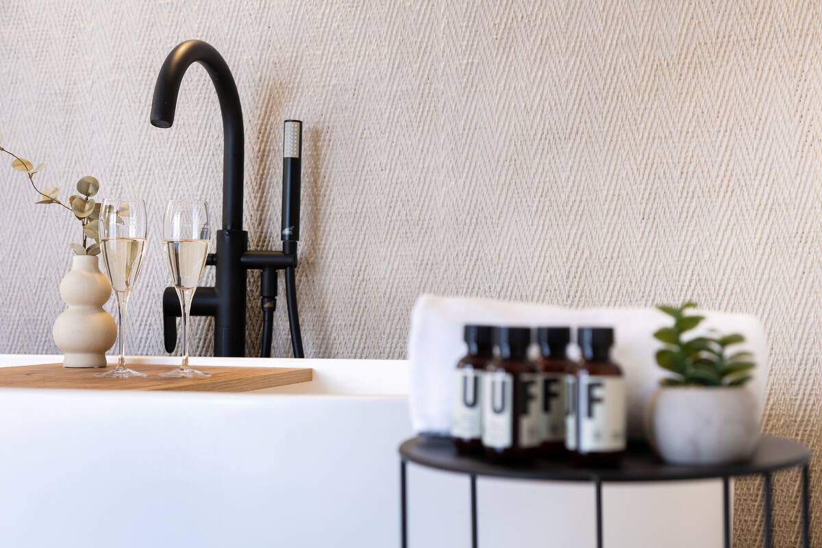 A modern bathroom with a black faucet, a white sink, and a small table with a potted plant and a bottle of UFF.