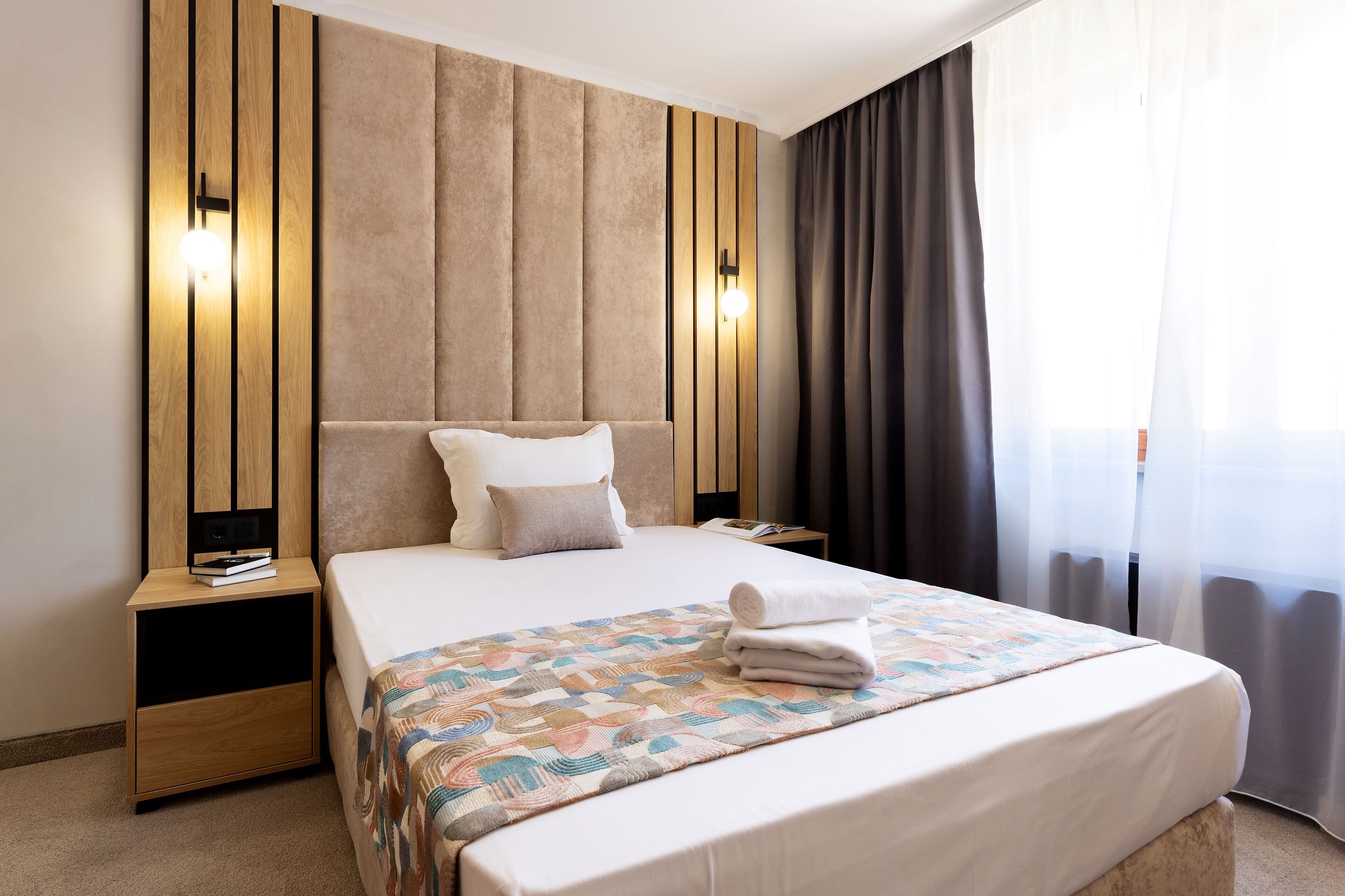 A hotel room with a large bed, a nightstand with a lamp, and a window with curtains.