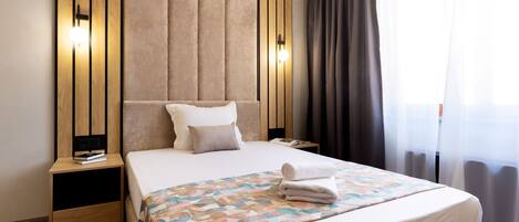A hotel room with a large bed, a nightstand with a lamp, and a window with curtains.