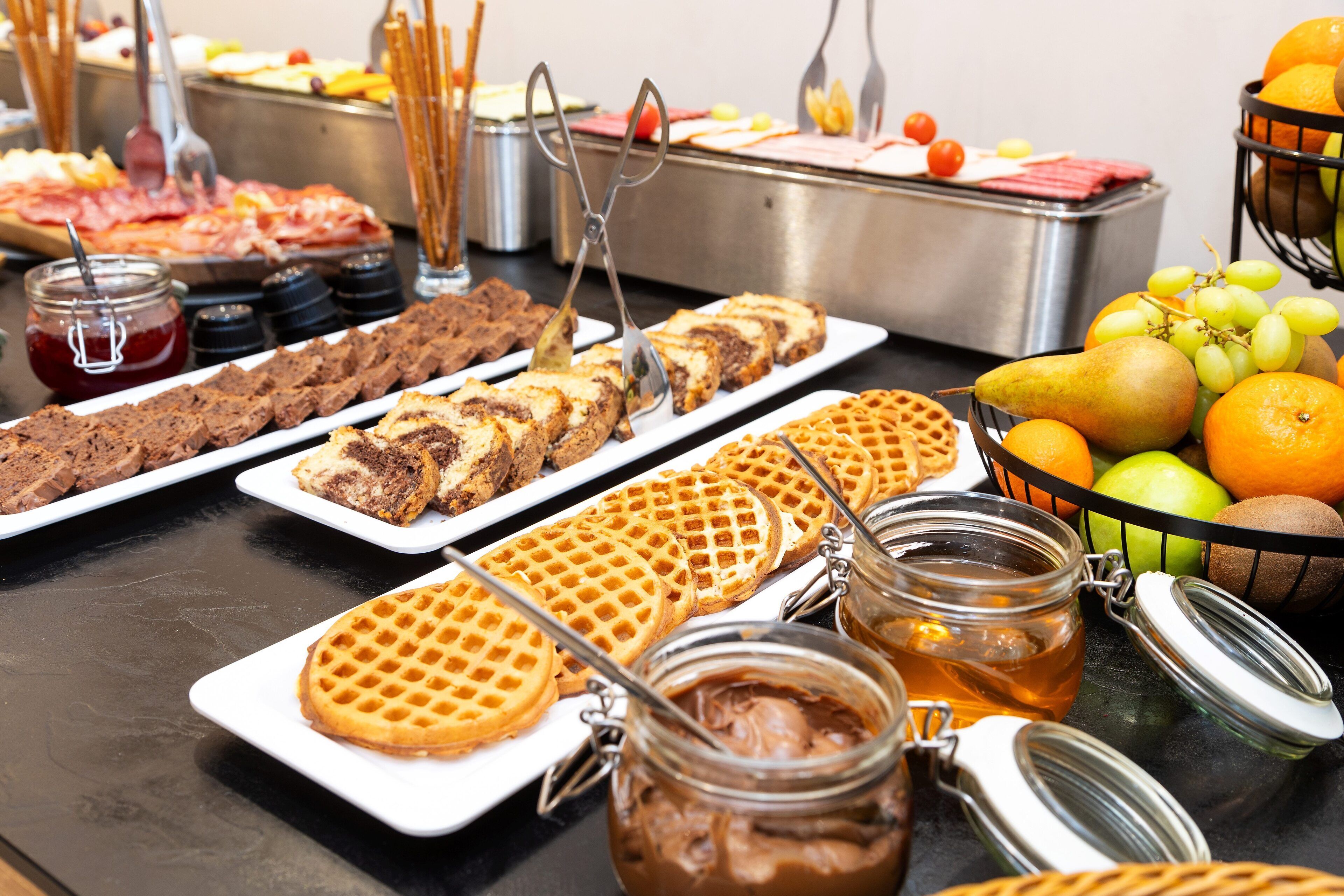 Un buffet proposant une variété de plats, notamment des gaufres, des pâtisseries et des fruits.