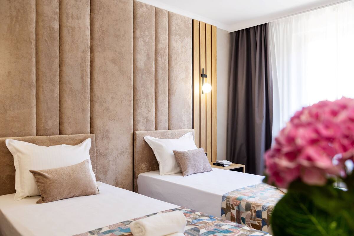 A hotel room with two beds, a wooden headboard, a nightstand, and a window with curtains.
