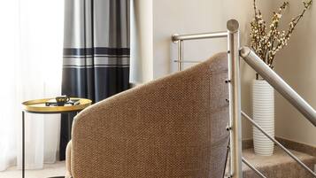 Een moderne woonkamer met een ruime, gestructureerde fauteuil, een klein rond tafeltje met een kopje en een trap met een leuning.