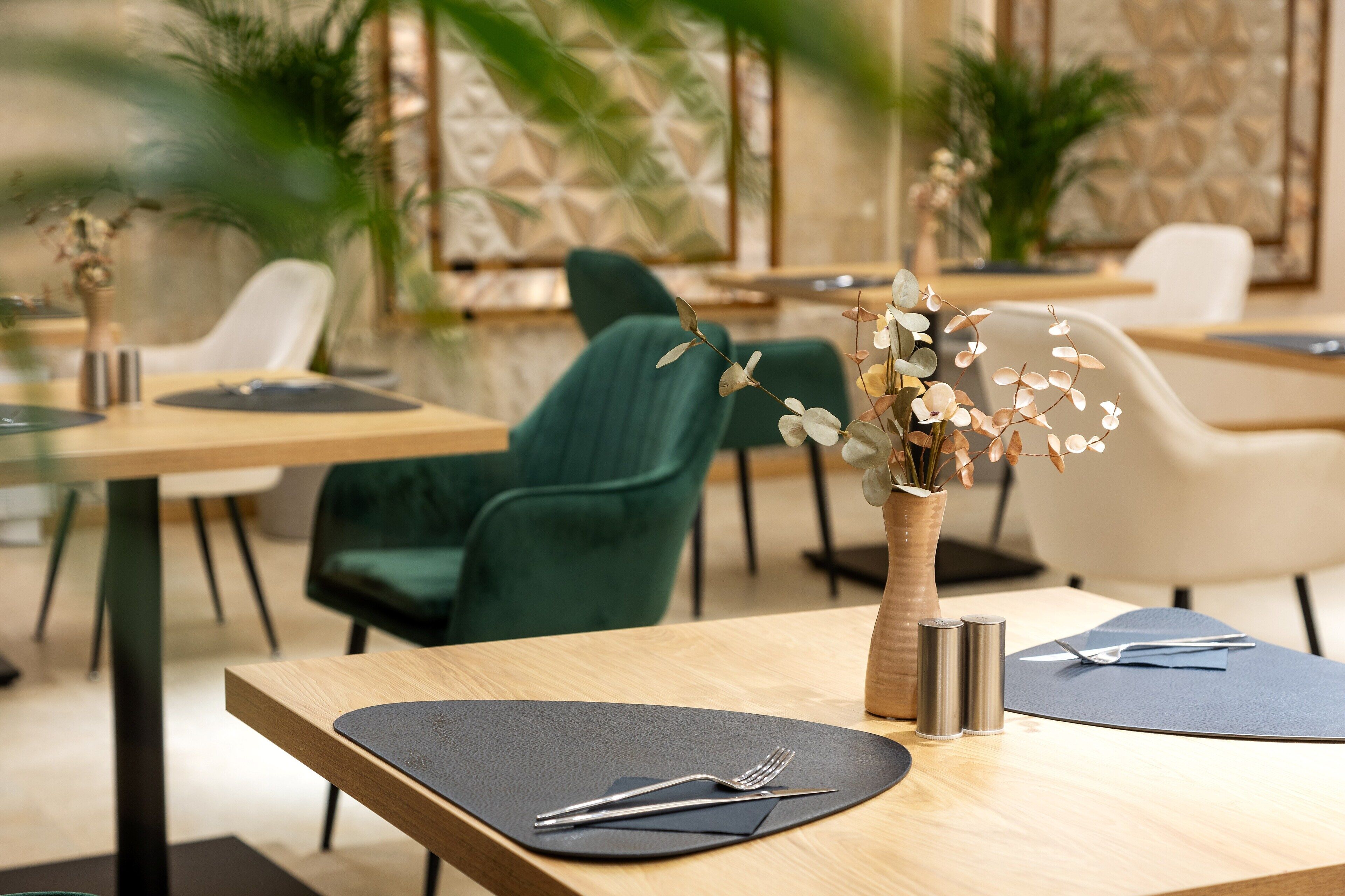 A restaurant with wooden tables, black placemats, and a vase with dried flowers.