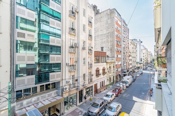 A multi-story urban street with various buildings, including a modern glass-fronted building and older residential structures.