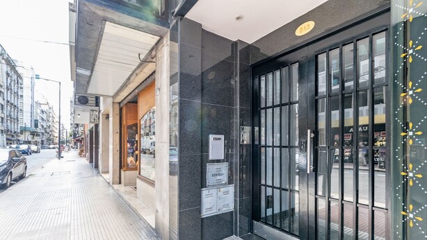 A building facade with a large glass door, a tiled sidewalk, and a visible street.