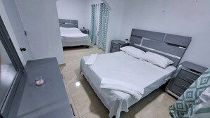 A hotel room with a large bed, a bedside table, a wardrobe, and a small table with a pink object.