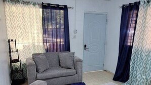 A living room with a grey sofa, ottoman, and a small table. There is a door and a curtain on the wall.
