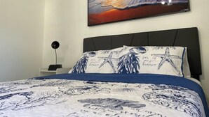 A bedroom with a bed, a nightstand, a wall-mounted painting of a sunset over the ocean, and a starfish pillow.
