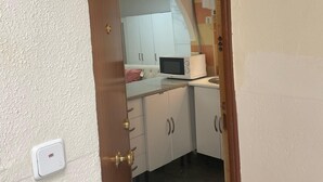 A narrow doorway leading into a kitchen with white cabinets, a microwave, and a tiled floor. - Your Perfect Escape Seasonal (Madrid)