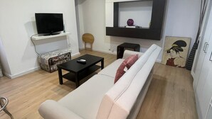 A modern living room with a sofa, a television, a small table, and a wall-mounted shelf. - Your Perfect Escape Seasonal (Madrid)