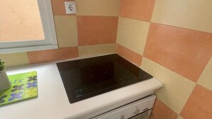 A compact kitchen with a black induction cooktop, a built-in oven, a washing machine, and a window with a view. - Your Perfect Escape Seasonal (Madrid)