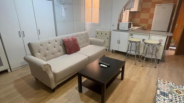A compact living space with a sofa, a coffee table, and a kitchenette area. - Your Perfect Escape Seasonal (Madrid)