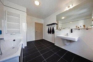 Un baño moderno con un lavamanos blanco, un espejo grande y un suelo con baldosas negras.
