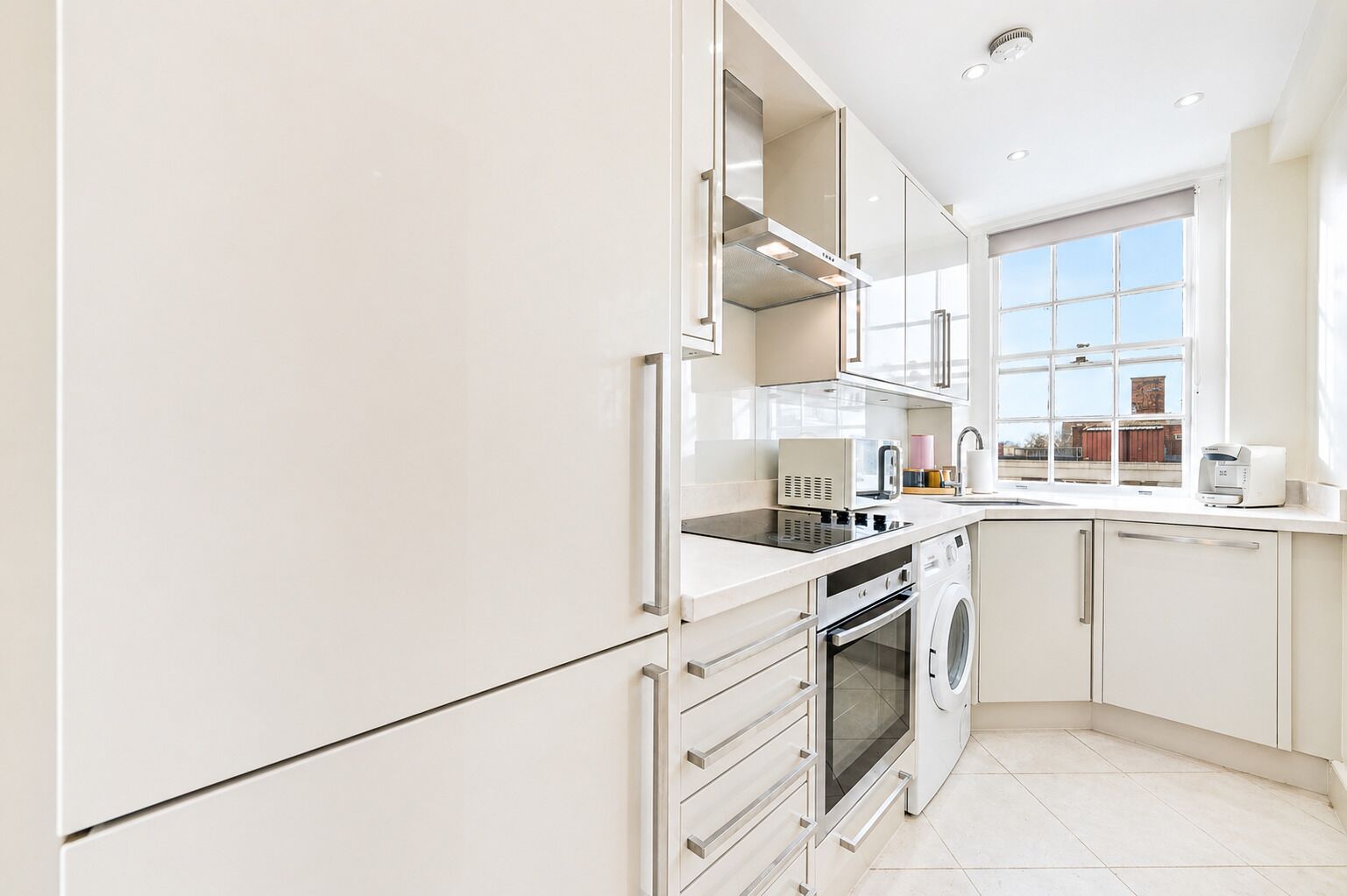 A modern kitchen with white cabinets, a built-in oven, a microwave, and a window with a view of buildings.