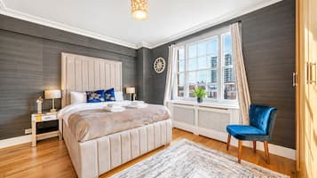 A bedroom with a large bed, bedside tables, a chair, a window with curtains, and a view of buildings.