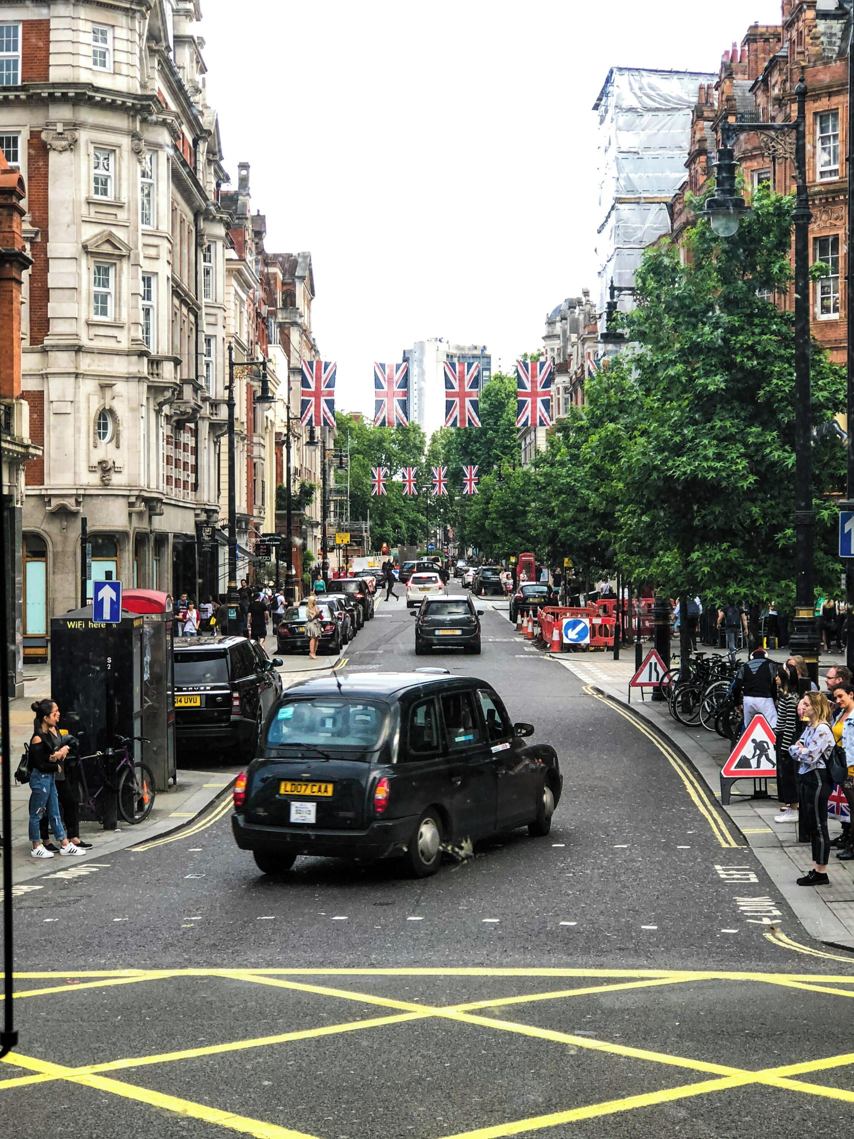 A street with buildings, flags, and cars.