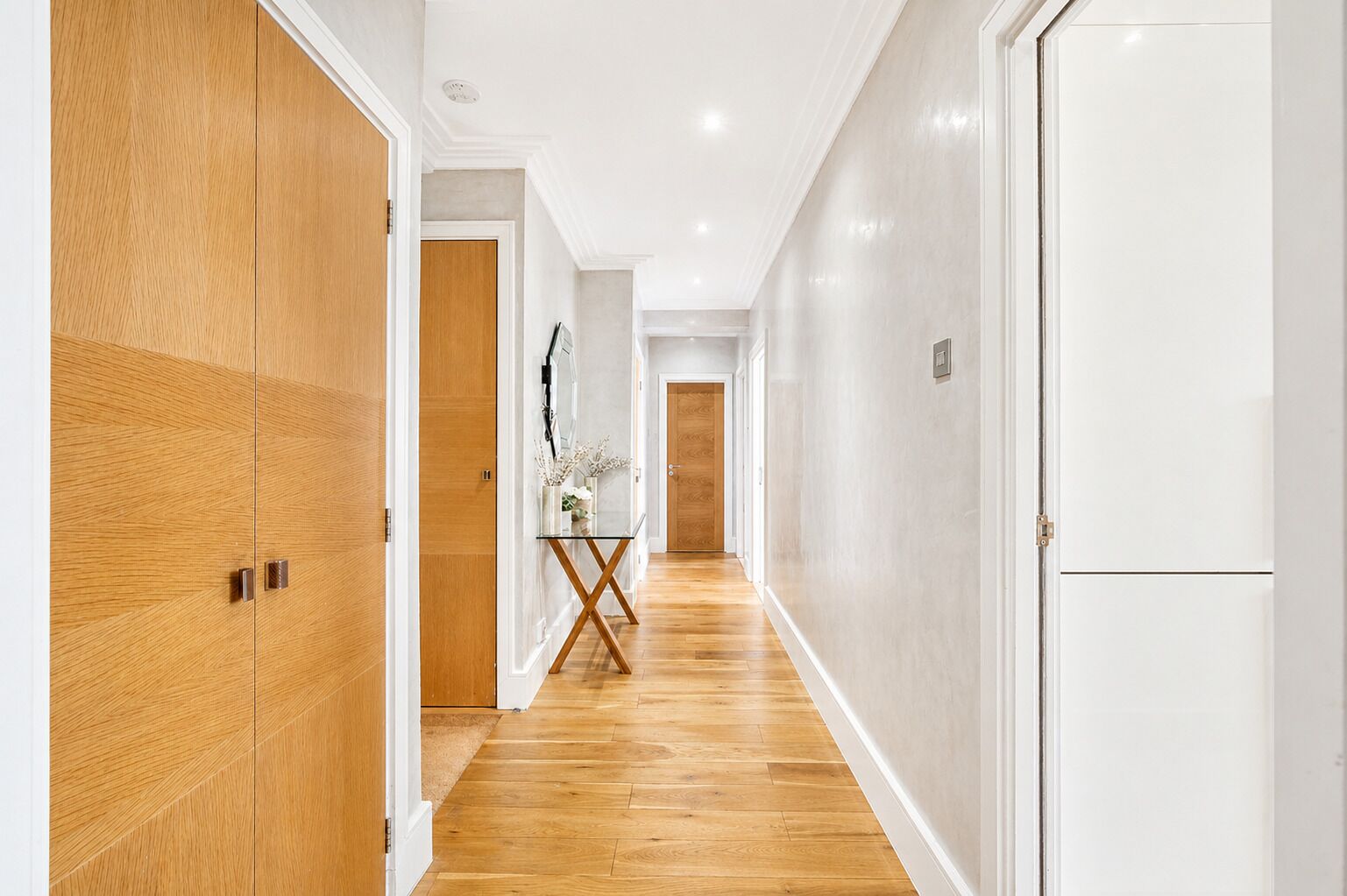 A hallway with wooden flooring, white walls, and doors.