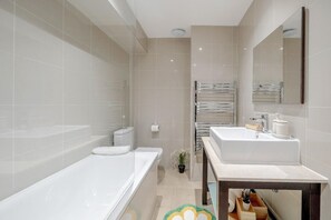 A modern bathroom with a bathtub, a sink, a toilet, and a mirror. - Forset Court Residences (London)